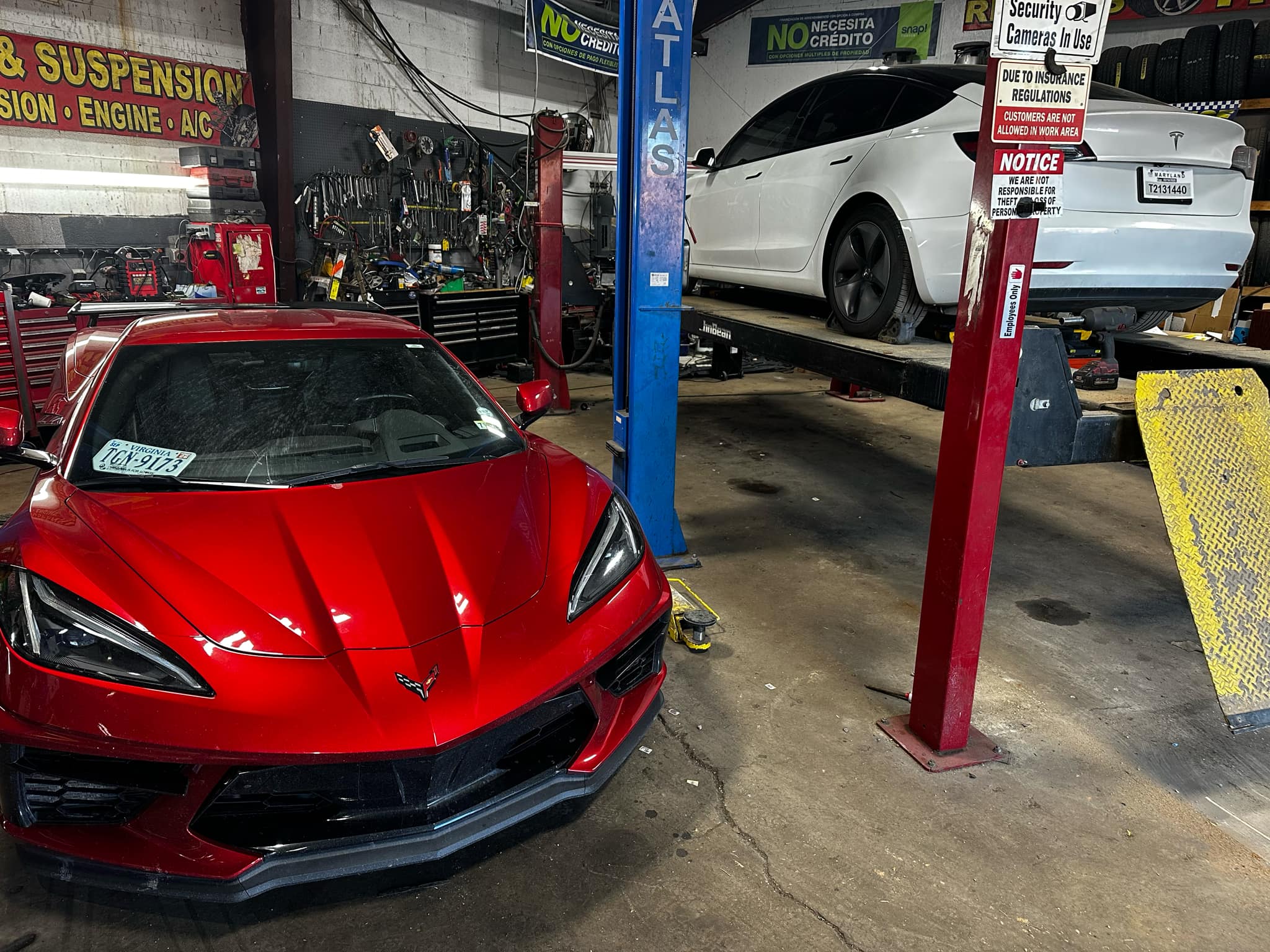 A garage with two cars on lifts, a red Corvette and a white Tesla.